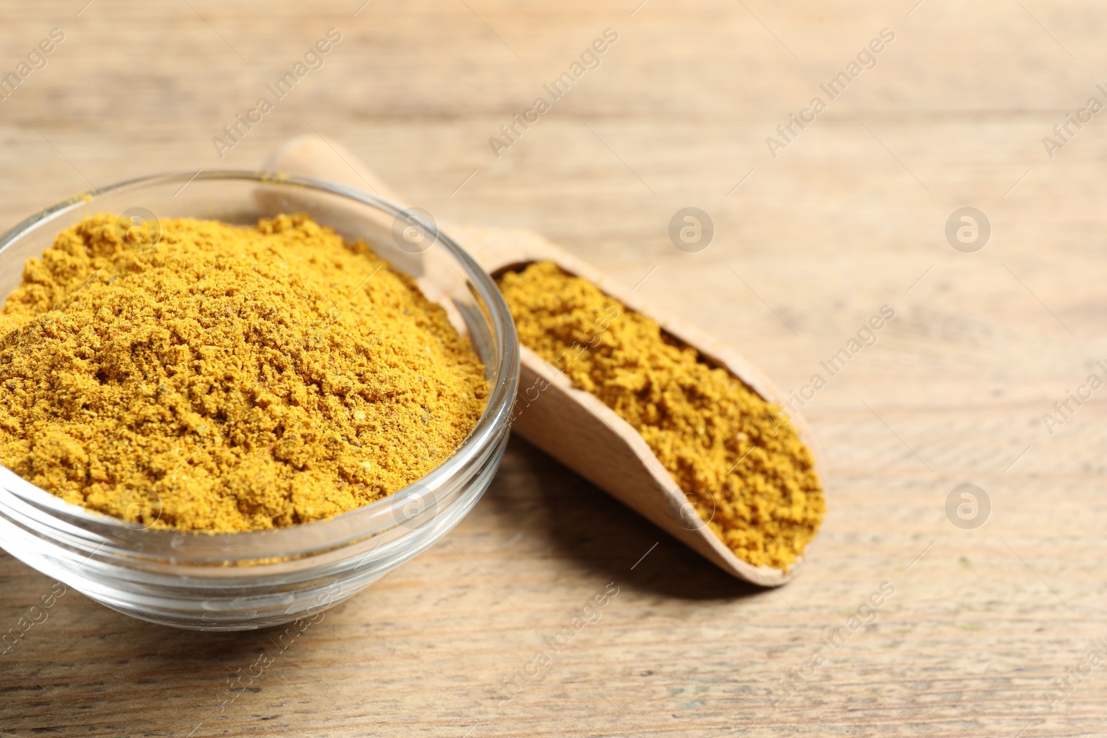 Photo of Curry powder in bowl and scoop on wooden table, closeup. Space for text