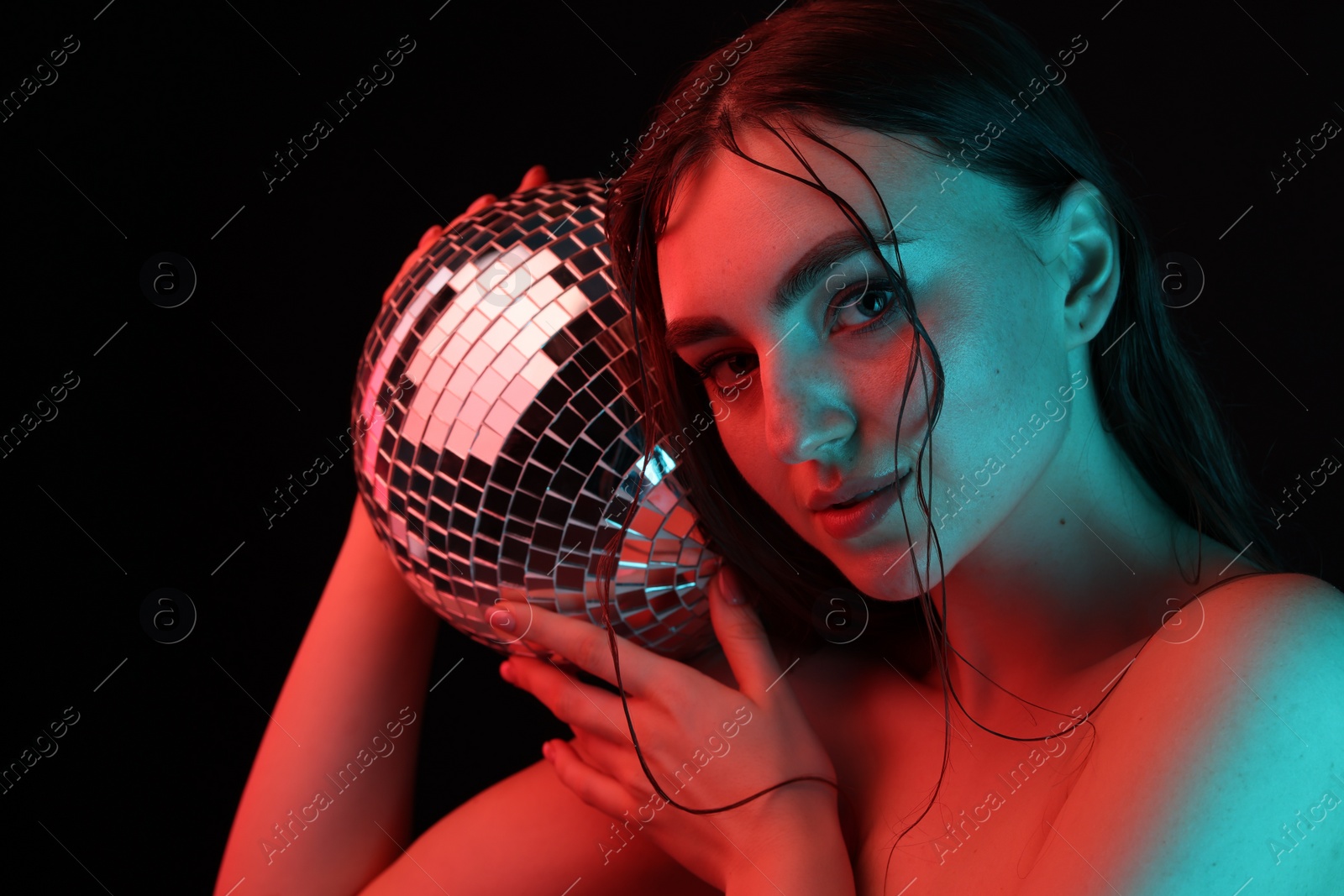 Photo of Beautiful woman with disco ball posing in neon lights against black background
