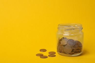 Photo of Glass jar with coins on yellow background, space for text