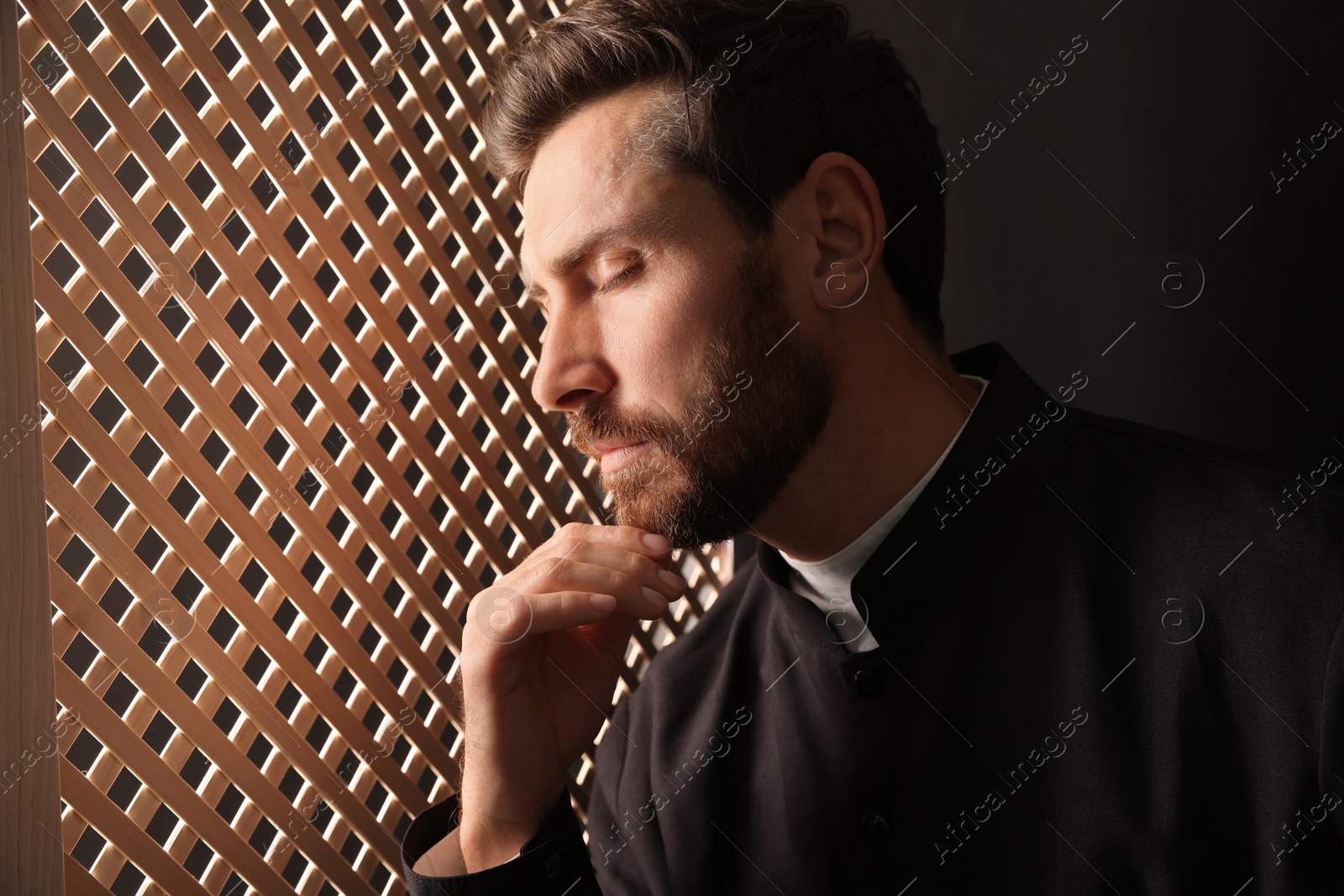 Photo of Catholic priest wearing cassock in confessional booth