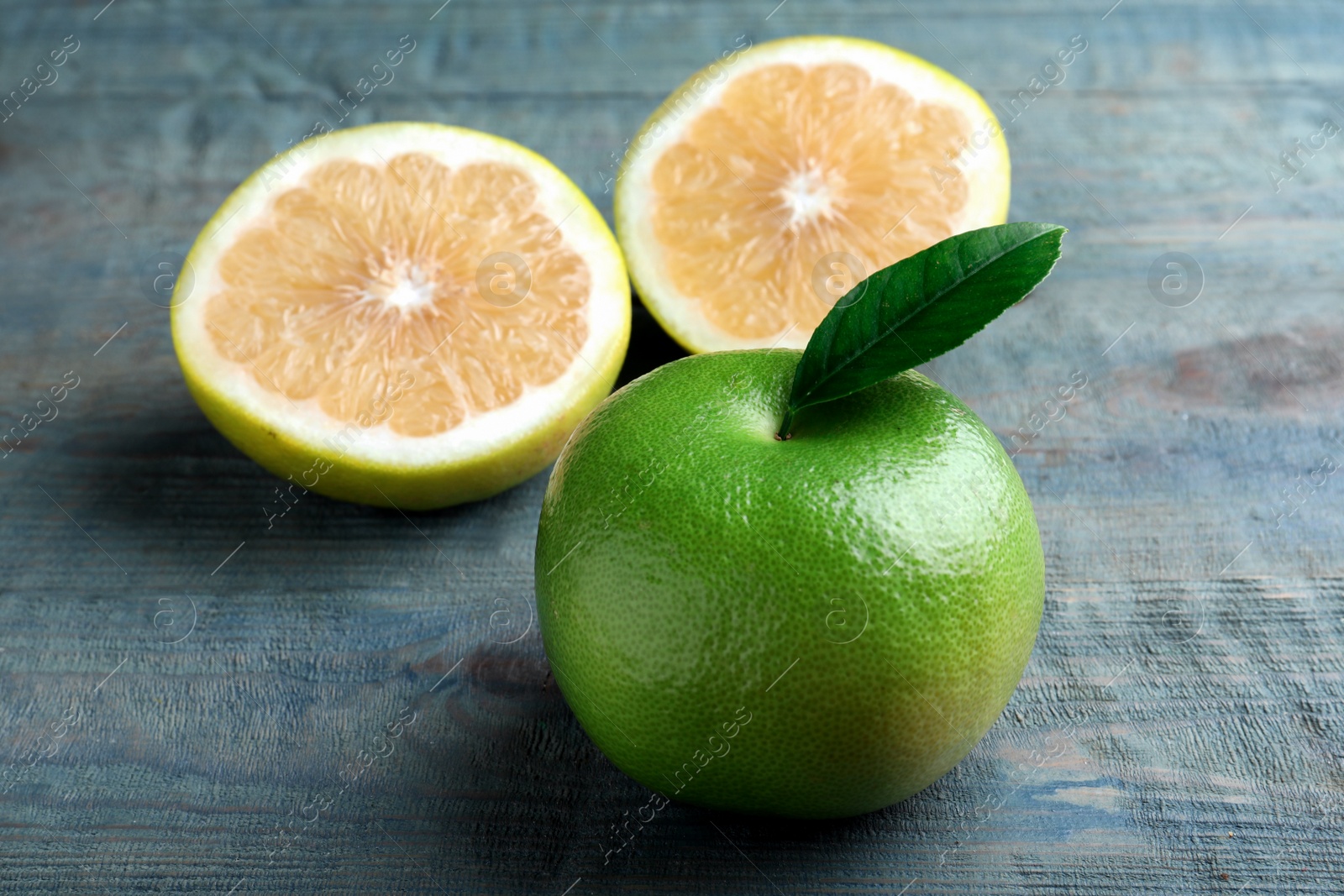 Photo of Whole and cut sweetie fruits on blue wooden table