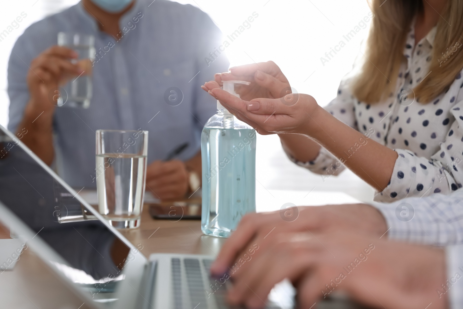 Photo of Office worker using hand sanitizer at table, closeup. Personal hygiene during COVID-19 pandemic