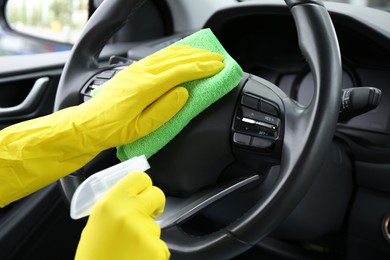 Woman cleaning steering wheel with rag in car, closeup