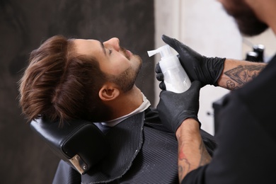 Professional hairdresser using talcum powder to calm client's skin after shaving in barbershop