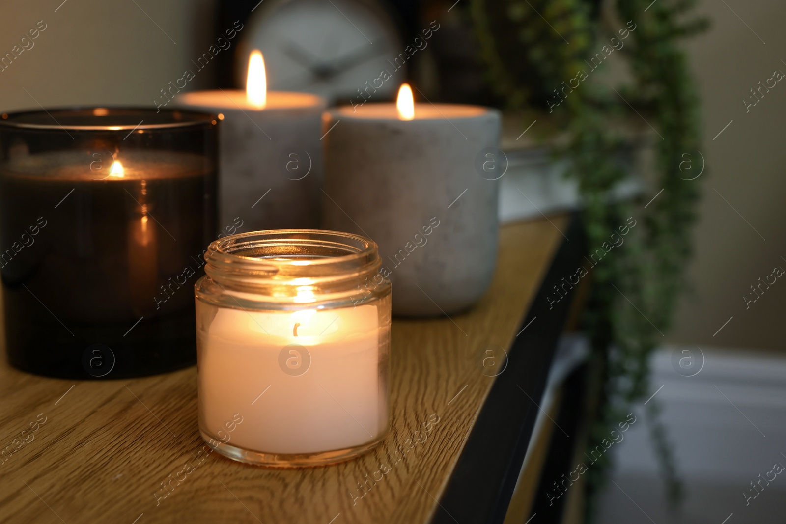 Photo of Lit candles in different holders on wooden table indoors. Space for text