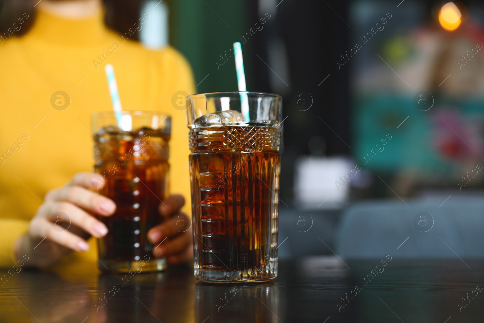 Photo of Glass of refreshing cola and blurred woman on background. Space for text