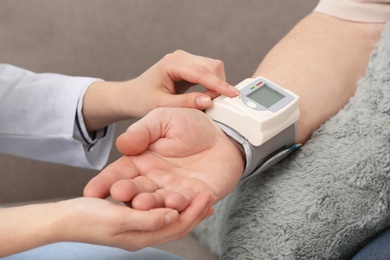Nurse measuring blood pressure of elderly man against grey background, closeup. Assisting senior generation