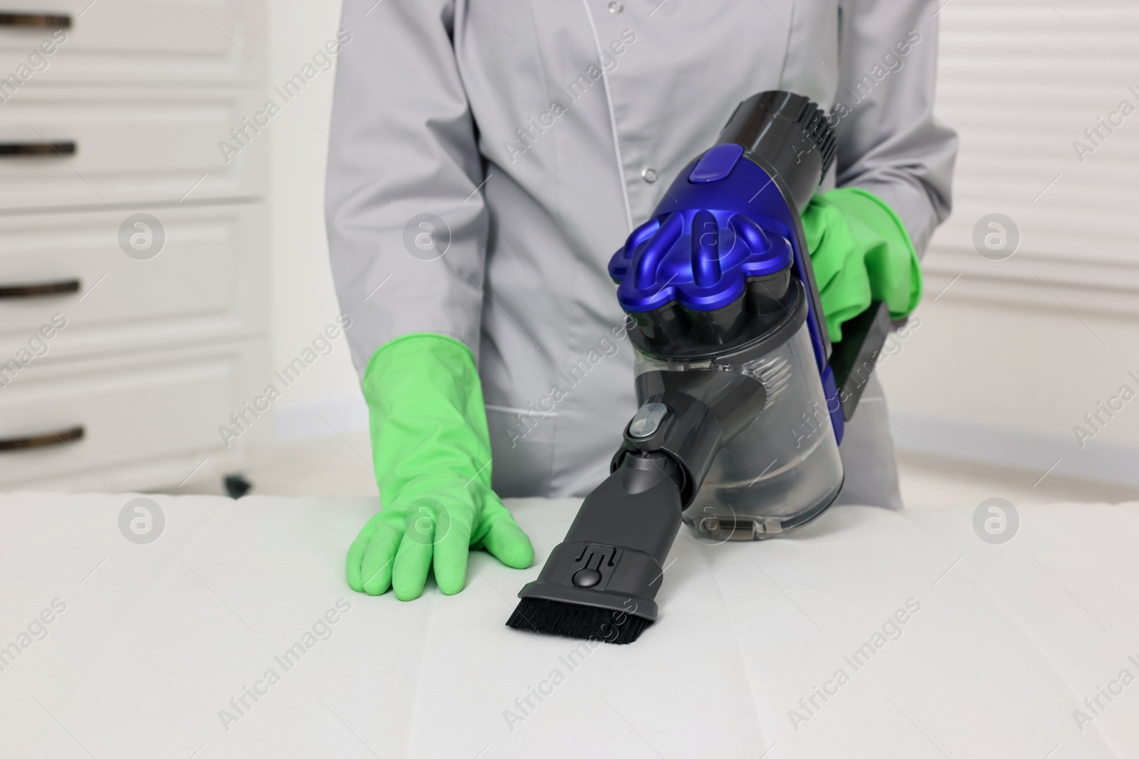 Photo of Woman in gloves disinfecting mattress with vacuum cleaner indoors, closeup