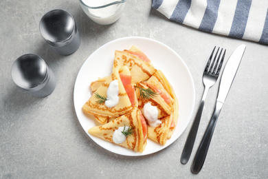 Photo of Delicious thin pancakes with salmon and sour cream on grey table, flat lay