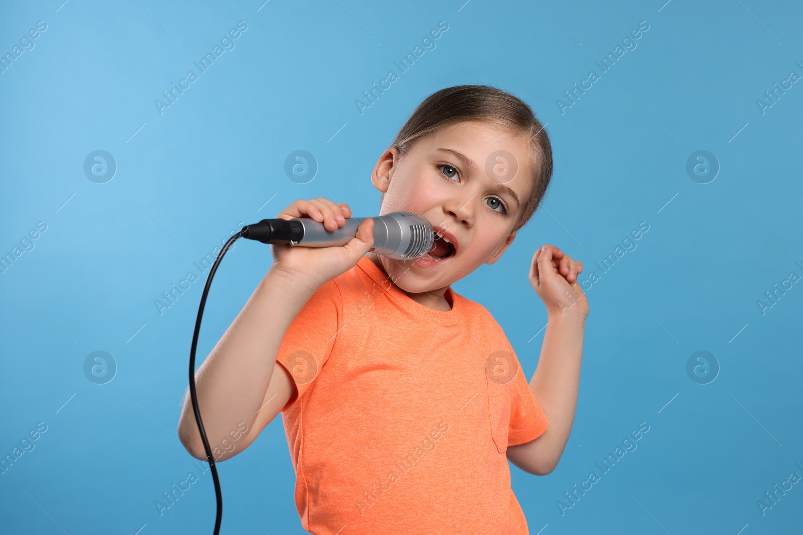 Photo of Cute little girl with microphone singing on light blue background