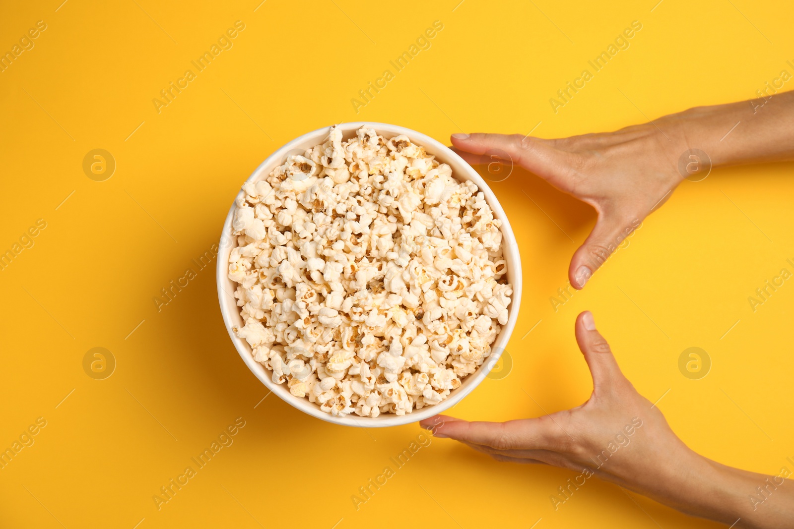 Photo of Woman with paper bucket of popcorn on color background, top view