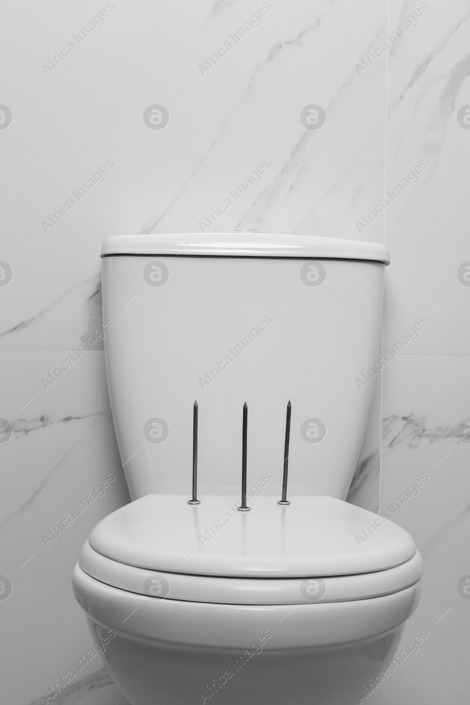 Photo of Toilet bowl with nails near marble wall. Hemorrhoids concept