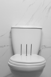 Photo of Toilet bowl with nails near marble wall. Hemorrhoids concept