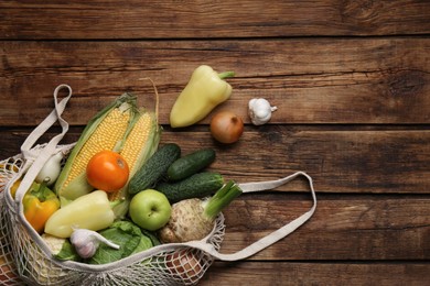 Photo of Different fresh vegetables in net bag on wooden table, flat lay and space for text. Farmer harvesting