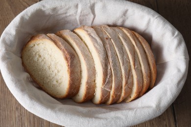 Photo of Fresh bread slices in basket on wooden table, top view