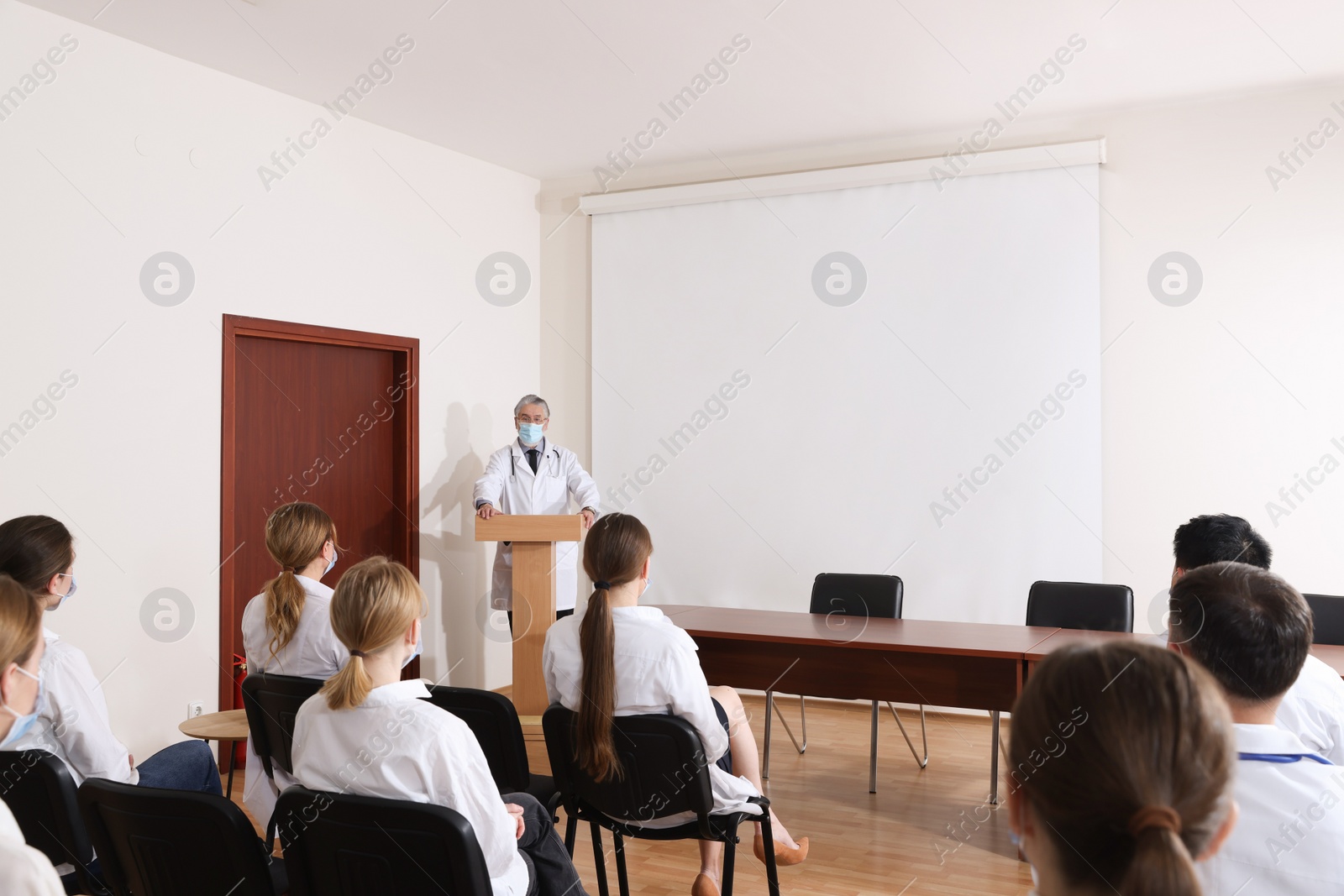 Photo of Senior doctor giving lecture near projection screen in conference room