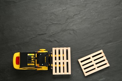 Toy forklift and wooden pallets on black table, flat lay. Space for text