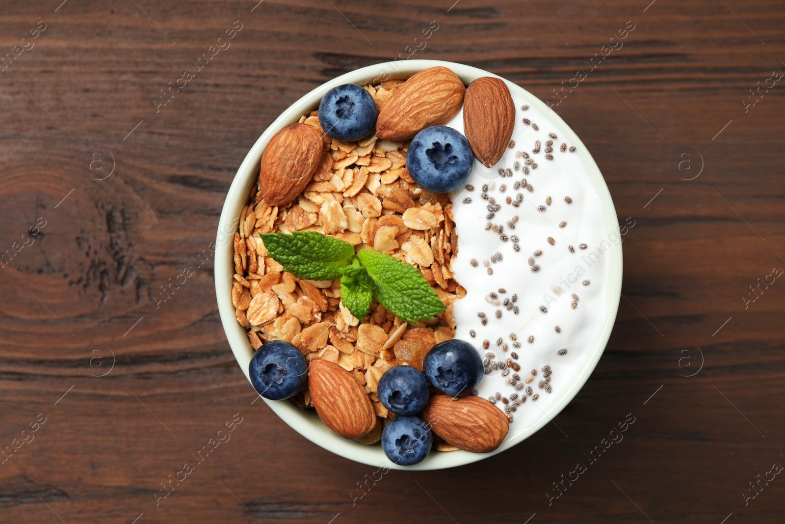 Photo of Tasty homemade granola with yogurt on wooden table, top view. Healthy breakfast