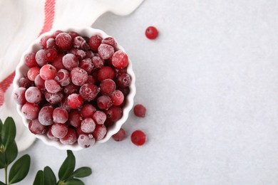 Photo of Frozen red cranberries in bowl and green leaves on light table, flat lay. Space for text