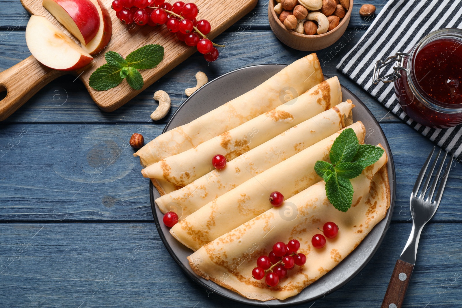 Photo of Delicious thin pancakes with berries on blue wooden table, flat lay