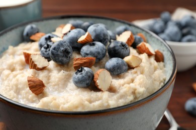 Photo of Tasty oatmeal porridge with blueberries and almond nuts in bowl on table, closeup