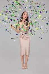 Beautiful woman with sparkler blowing kiss under falling confetti on grey background