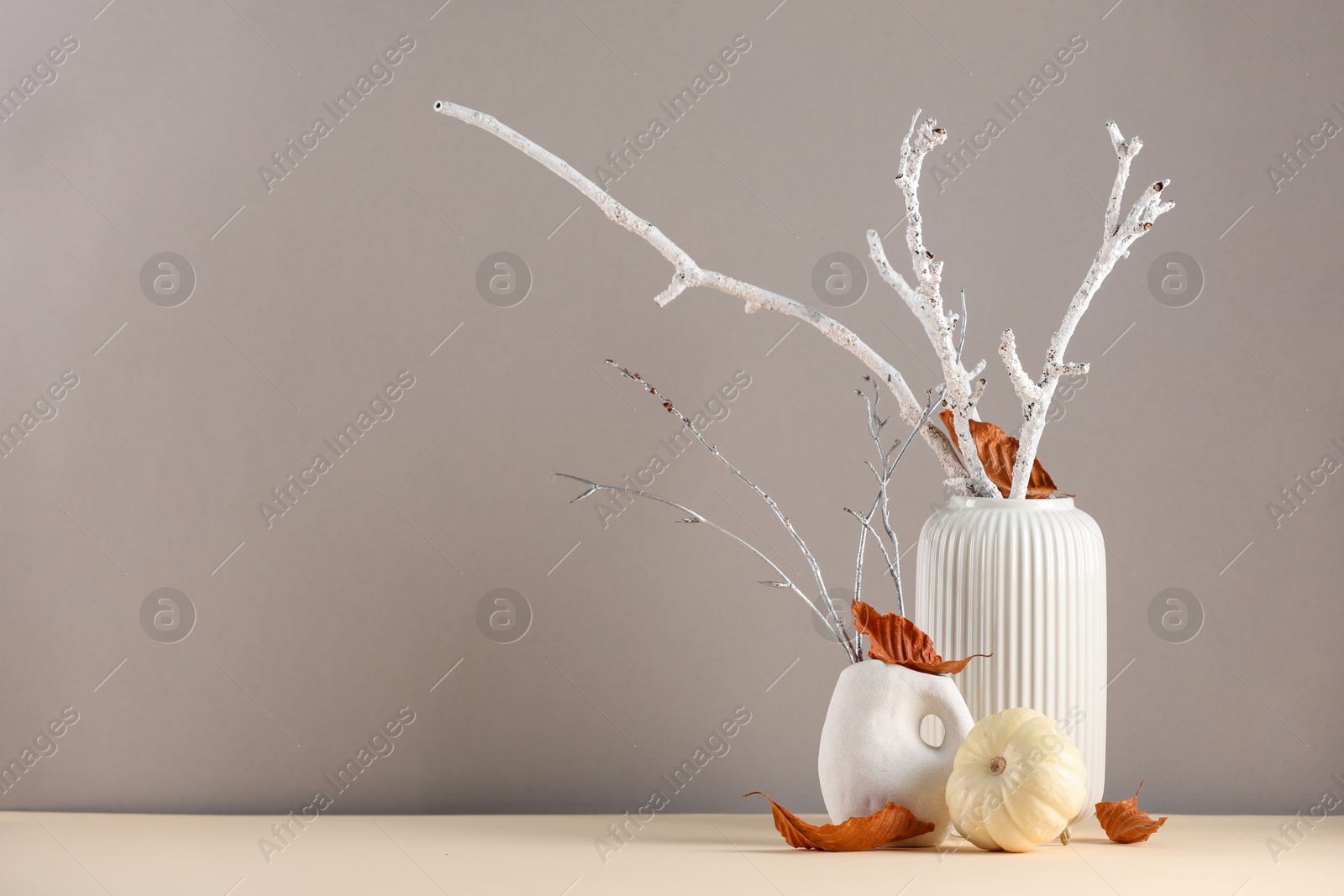 Photo of Composition with beautiful autumn leaves, tree branches and pumpkin on table against light gray background, space for text