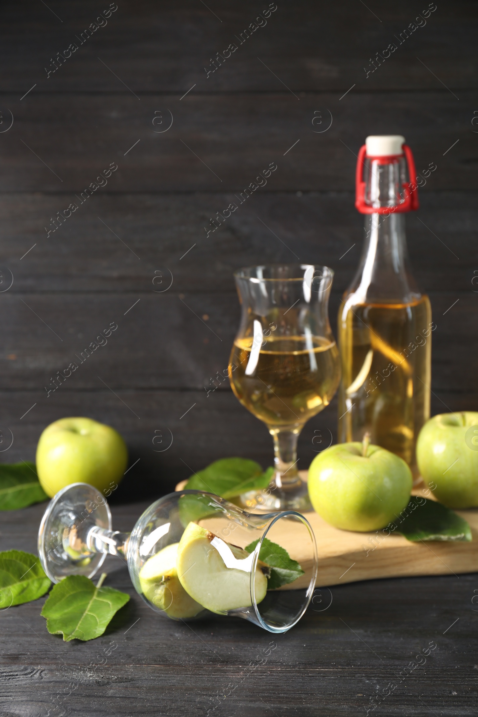 Photo of Delicious cider and apples with green leaves on black wooden table