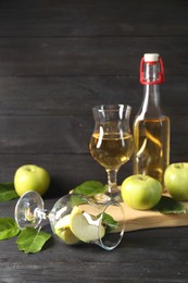 Photo of Delicious cider and apples with green leaves on black wooden table