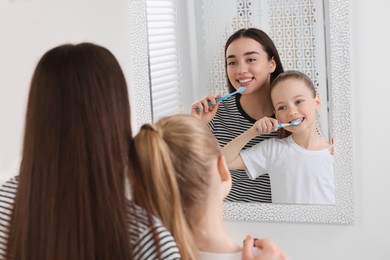 Mother and her daughter brushing teeth together near mirror indoors