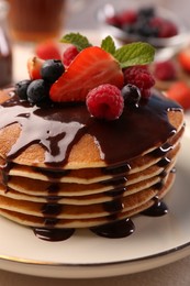 Stack of tasty pancakes with fresh berries, chocolate sauce and mint on white plate, closeup