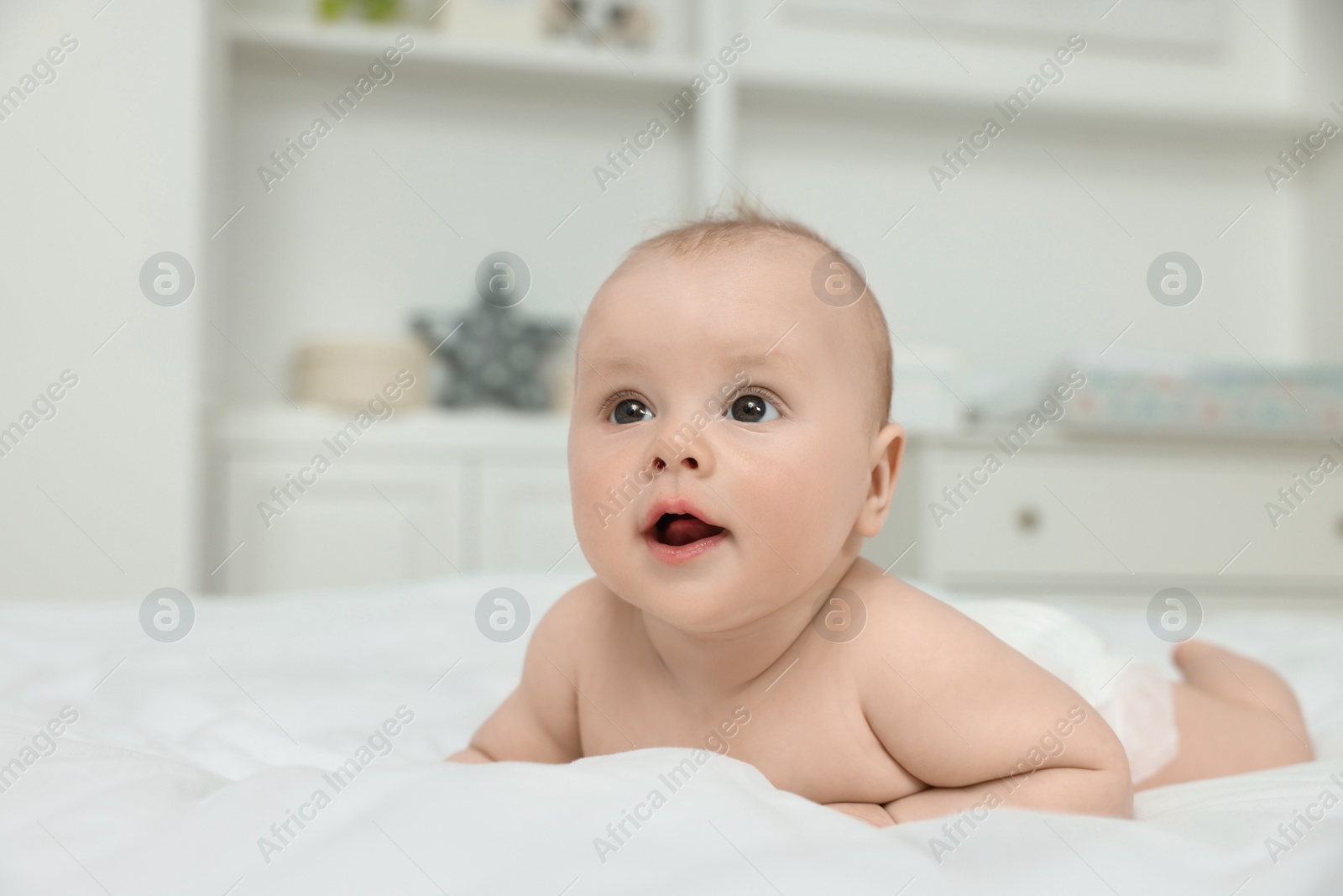 Photo of Cute baby lying on white bed at home, space for text