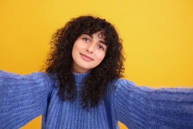 Beautiful young woman taking selfie on orange background