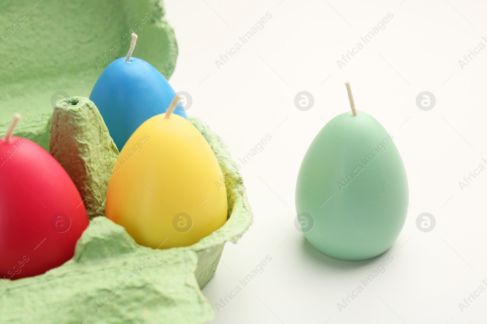 Photo of Colorful egg shaped candles in carton on white table, closeup. Easter decor