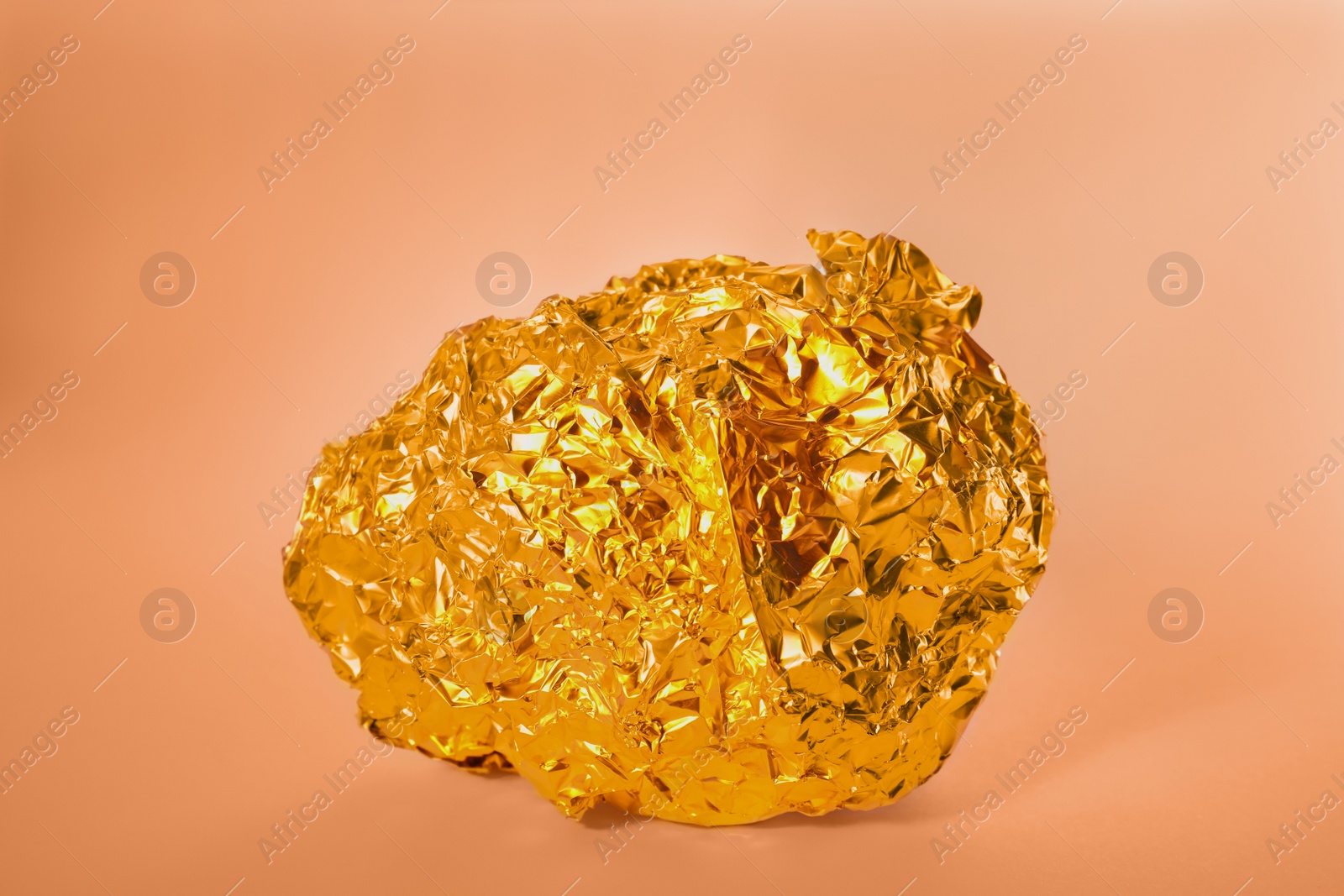 Photo of Crumpled ball of gold foil on light background, color tone effect