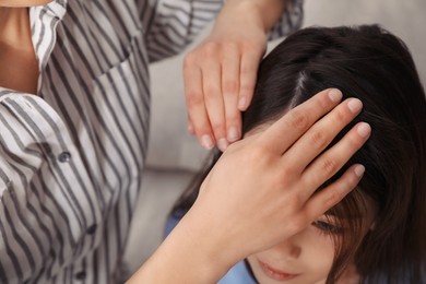 Photo of Mother examining her daughter's hair indoors. Anti lice treatment