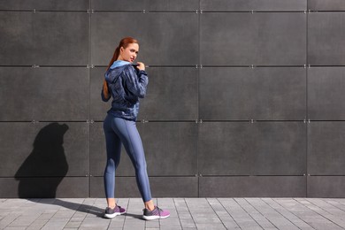 Photo of Beautiful woman in stylish gym clothes near dark grey wall on street, space for text