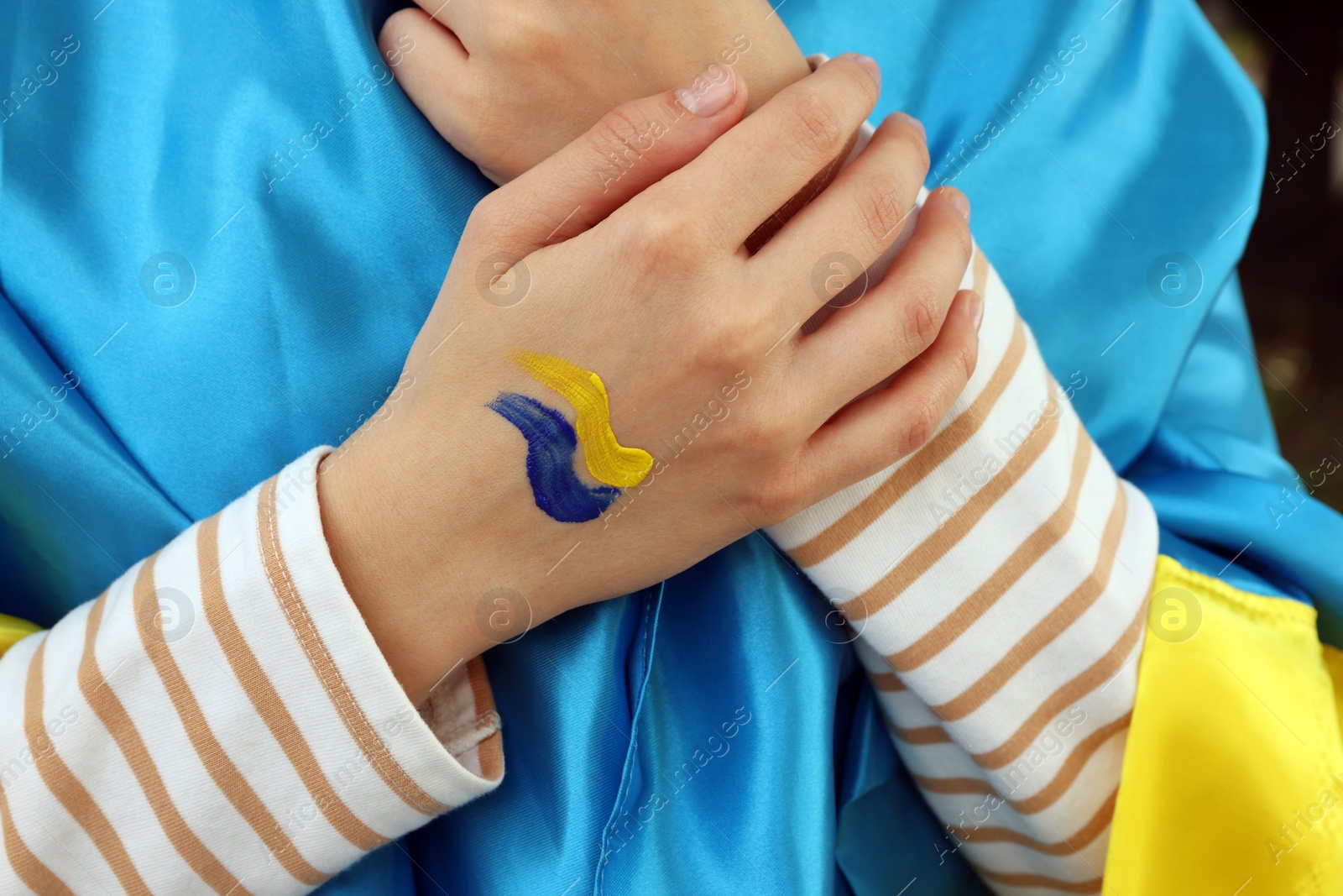 Photo of Woman with drawing of Ukrainian flag on hand against blurred background, closeup