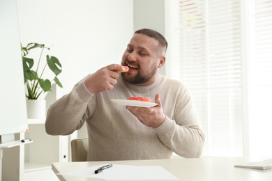 Photo of Lazy overweight office employee with donuts at workplace