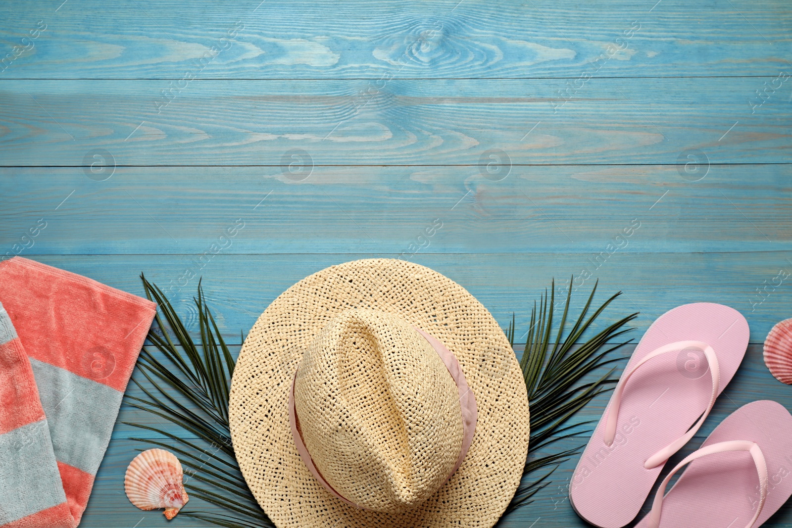 Photo of Beach towel, straw hat and flip flops on light blue wooden background, flat lay. Space for text