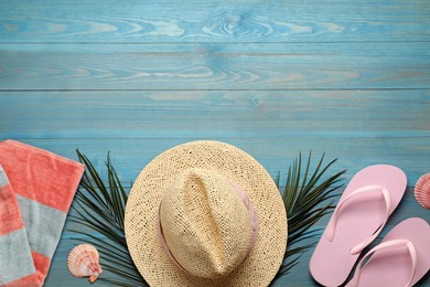 Beach towel, straw hat and flip flops on light blue wooden background, flat lay. Space for text