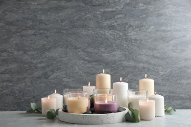 Set of burning candles with eucalyptus on table against grey marble background. Space for text