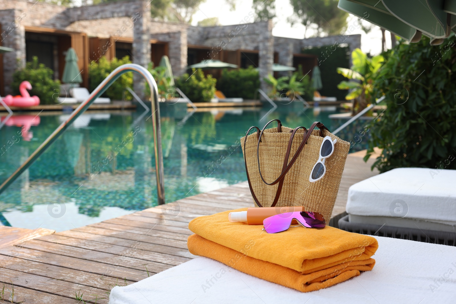 Photo of Wicker bag with beach accessories on sunbed near outdoor swimming pool, space for text. Luxury resort