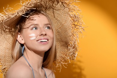 Photo of Beautiful young woman in straw hat with sun protection cream on her face against orange background. Space for text