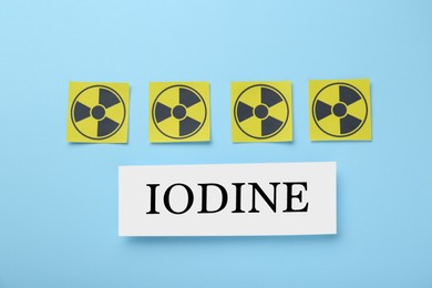 Photo of Paper note with word Iodine and radiation signs on light blue background, flat lay