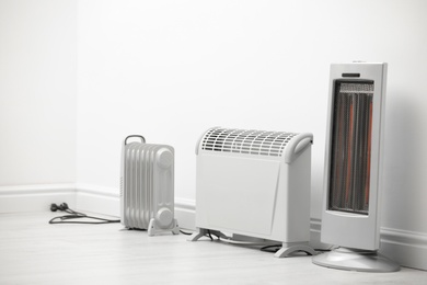 Different electric heaters near white wall indoors