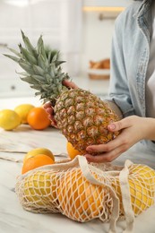 Photo of Woman taking pineapple out from string bag at light marble table, closeup