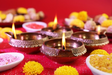 Photo of Diwali celebration. Diya lamps, bright rangoli and chrysanthemum flowers on shiny red table, closeup