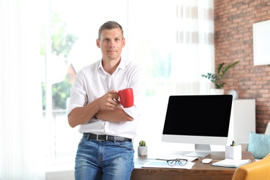 Photo of Young man with cup of coffee near table in office. Time to work