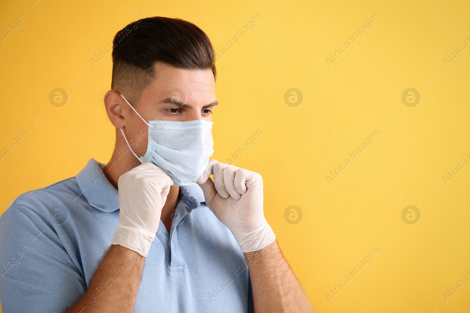 Photo of Man in medical gloves putting on protective face mask against yellow background. Space for text
